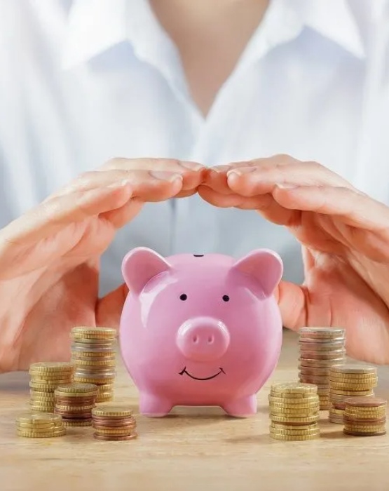 two hands over a piggy bank surrounded by coins