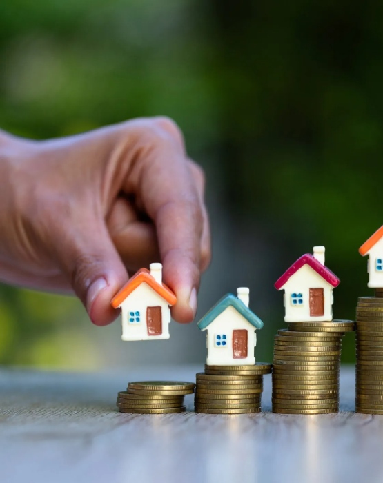 a hand placing small model houses on stacked coins