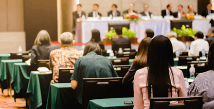 An audience of people listening to the Board of Directors at a shareholders meeting.