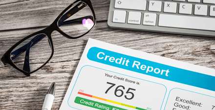 A credit report lying on a desktop with a pair of black-rimmed glasses, a pen, and keyboard.