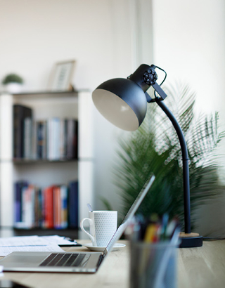 a desk lamp, coffee mug and laptop on a desk